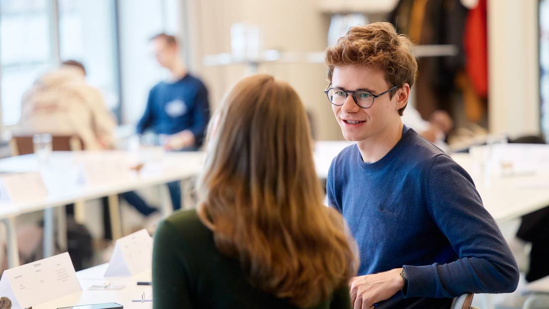 Ein Teilnehmer unterhält sich mit einer Teilnehmerin, beide sitzen im Workshopraum