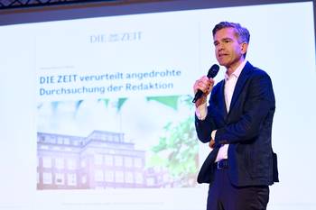 Foto von Nils von der Kall auf der Bühne. Im Hintergrund eine Präsentation auf der zu lesen ist: Die ZEIT verurteilt angedrohte Durchsuchung der Redaktion