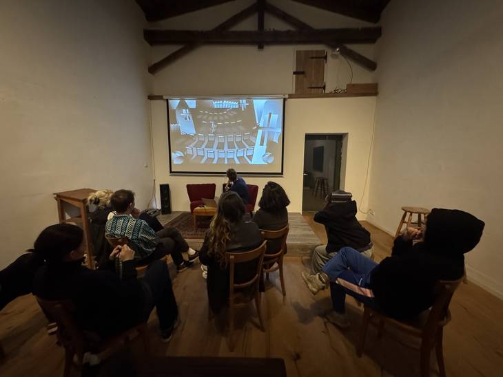 Eine Gruppe Menschen sitzt auf Stühlen und schaut eine Präsentation auf einer Leinwand an.