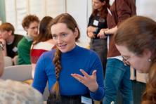 Fotografie einer Frau, die auf einem Stuhl sitzt und etwas erklärt.